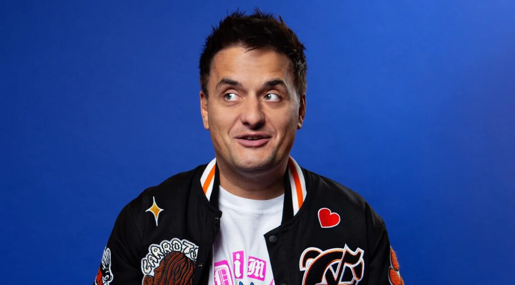 George Zak headshot in letterman jacket against a blue background