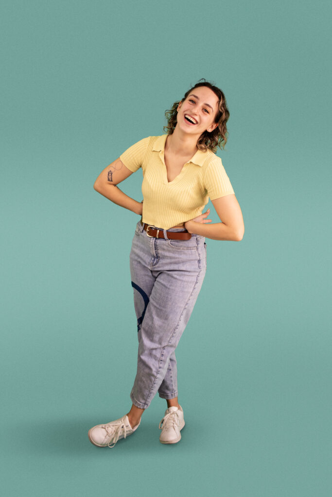 Jamie Lerner poses standing in yellow shirt against teal background